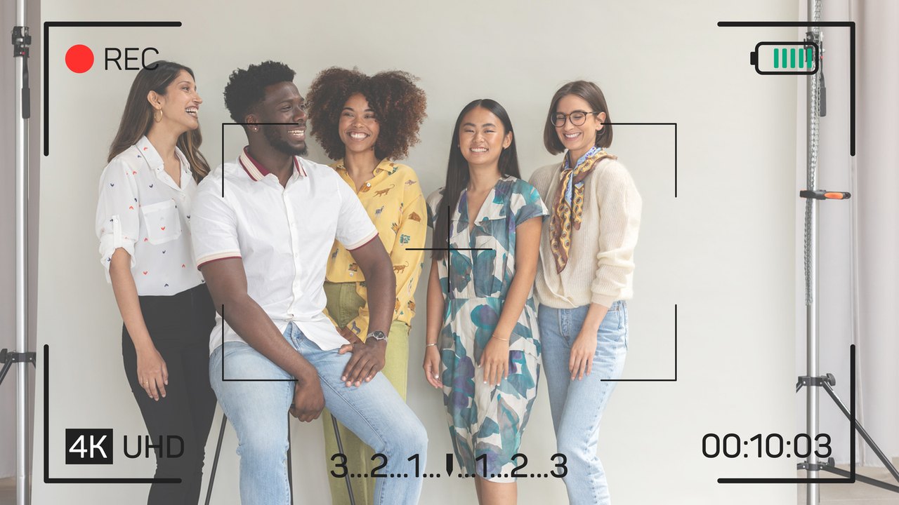Screenjack showing a camera's live view: five people posing in front of a white studio backdrop, with the camera's own framing brackets, record light, battery, and timecode drawn over the picture.